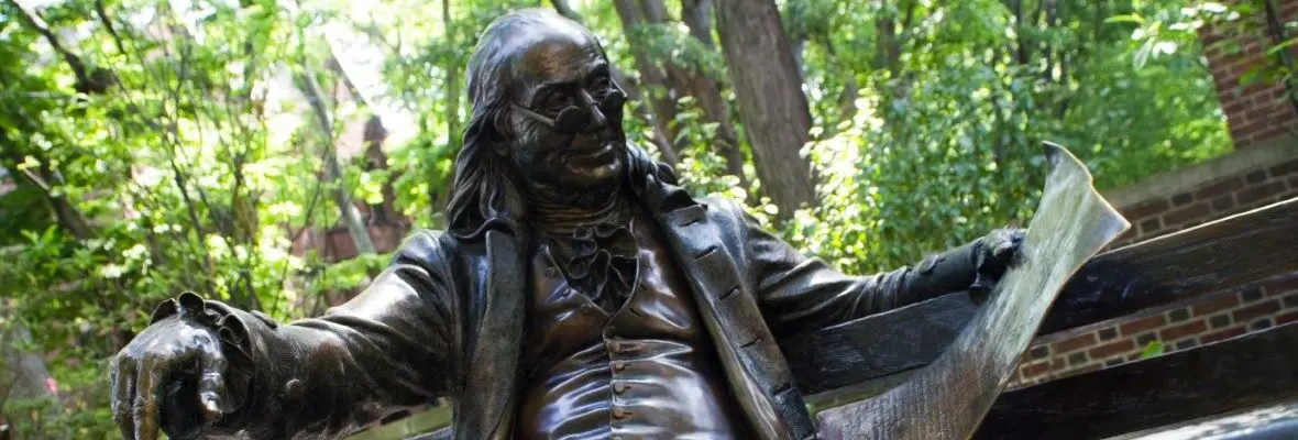 statue of Benjamin Franklin reading on bench outside