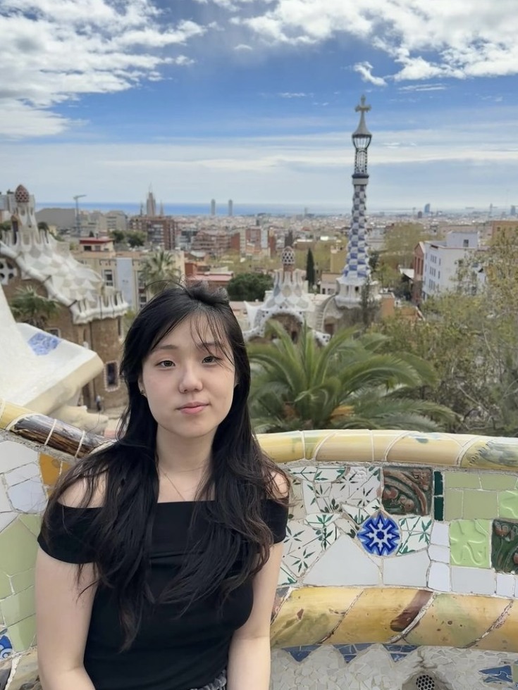 a young woman in a black top sitting on a tiled bench in a city.