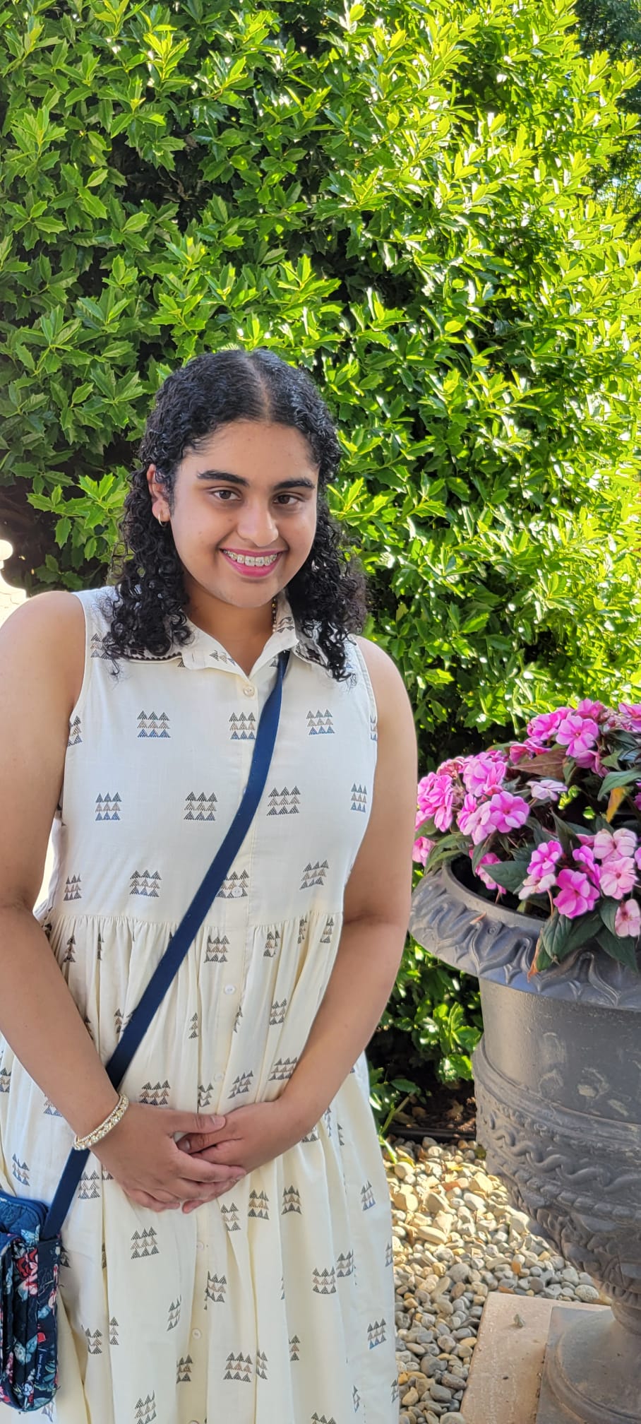 a woman standing outside in front of a green bush wearing a white dress